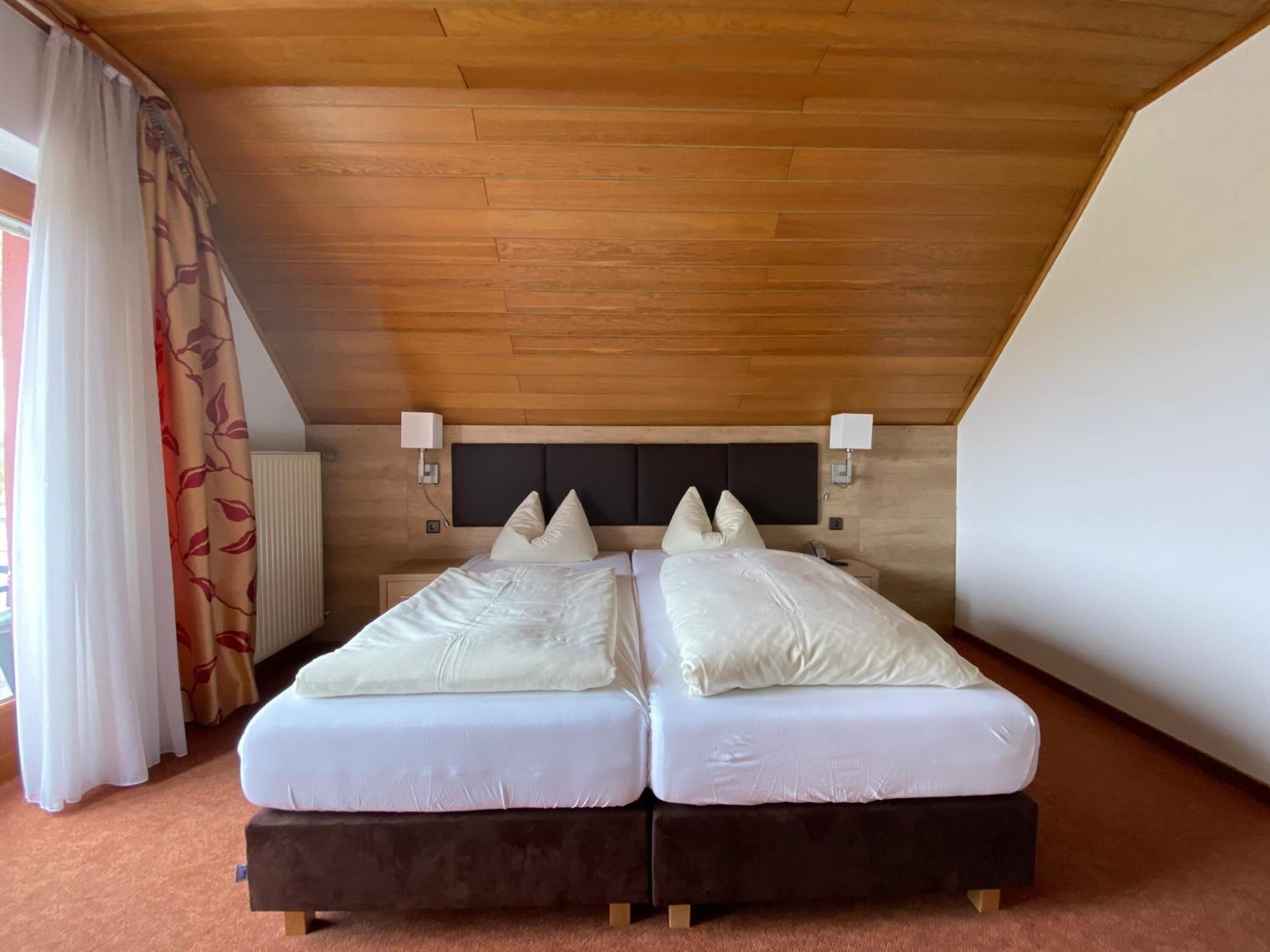 Habitación con dos camas individuales, techo de madera, dos mesitas de noche y un radiador.
