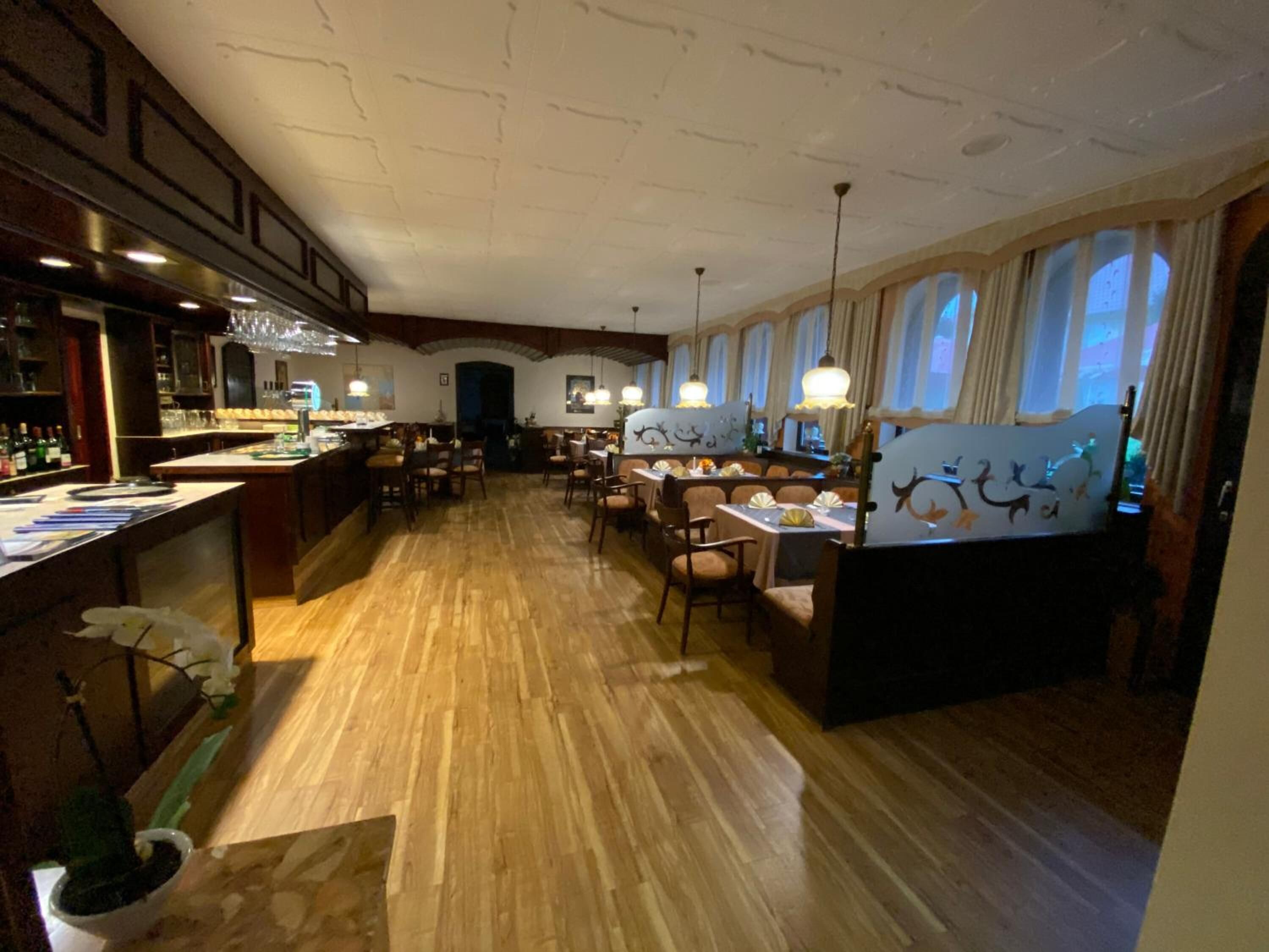 Un restaurante con suelos de madera, una zona de bar y mesas con sillas.