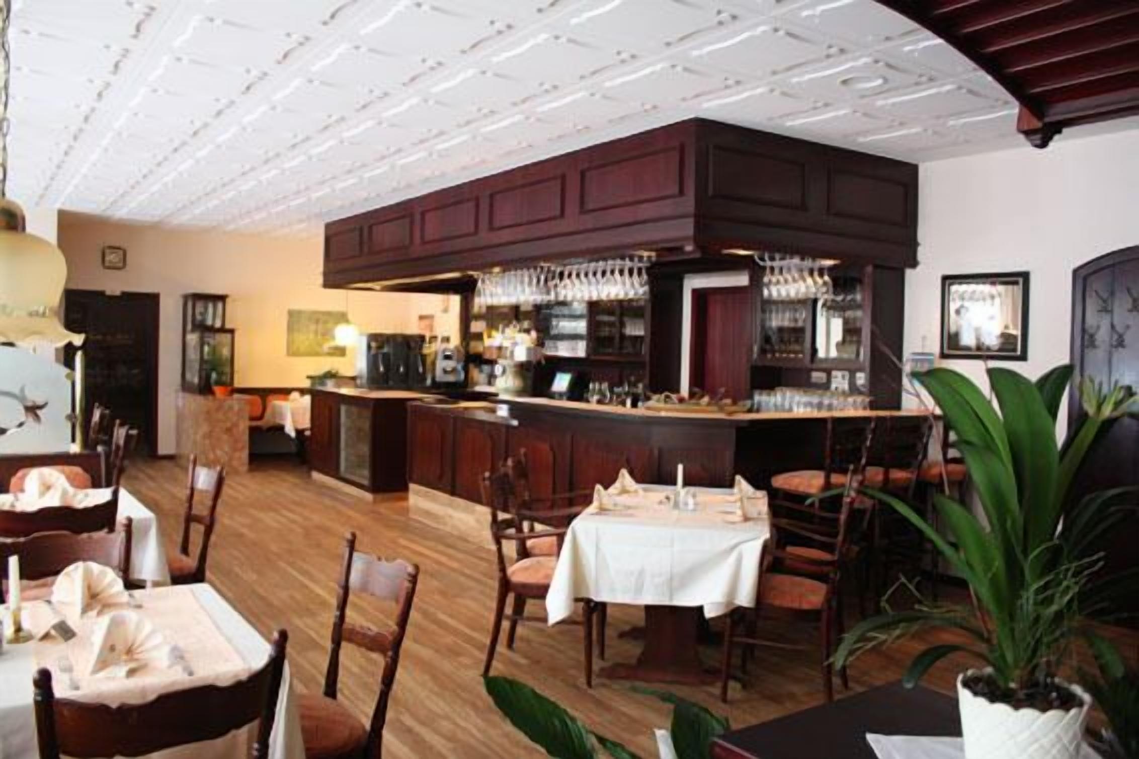 A restaurant with wooden flooring, a bar area with a counter and bar stools, and a dining area with tables and chairs.