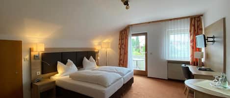Una camera d'albergo con un letto grande, comodini con lampade, una scrivania con sedia, una TV e un balcone con tende.