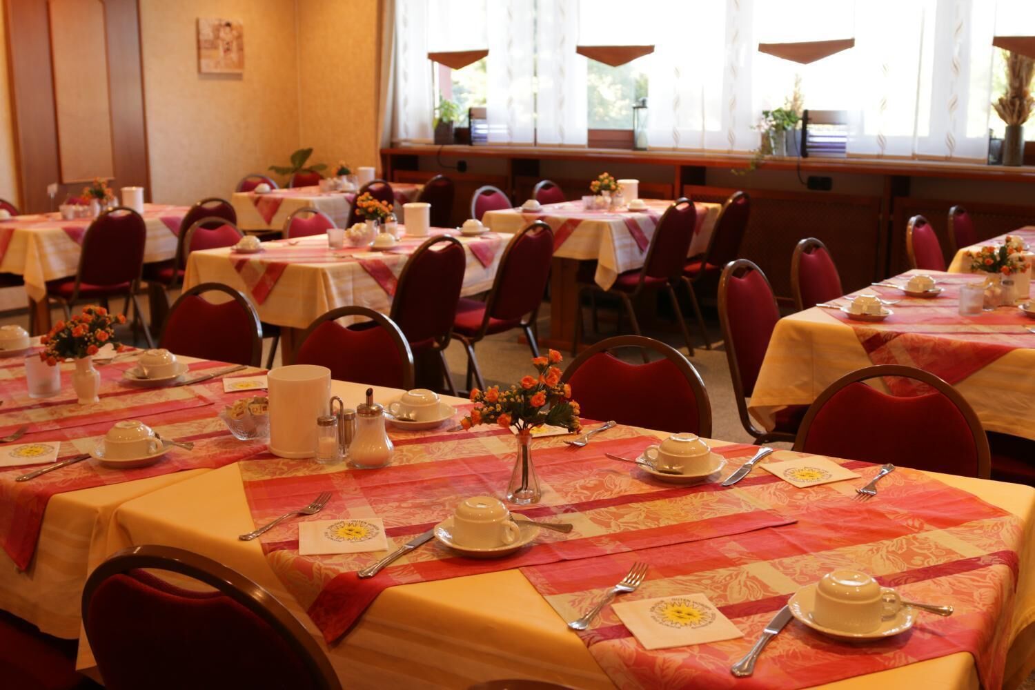 A dining area with multiple tables set for service, each with a tablecloth, chairs, and tableware.