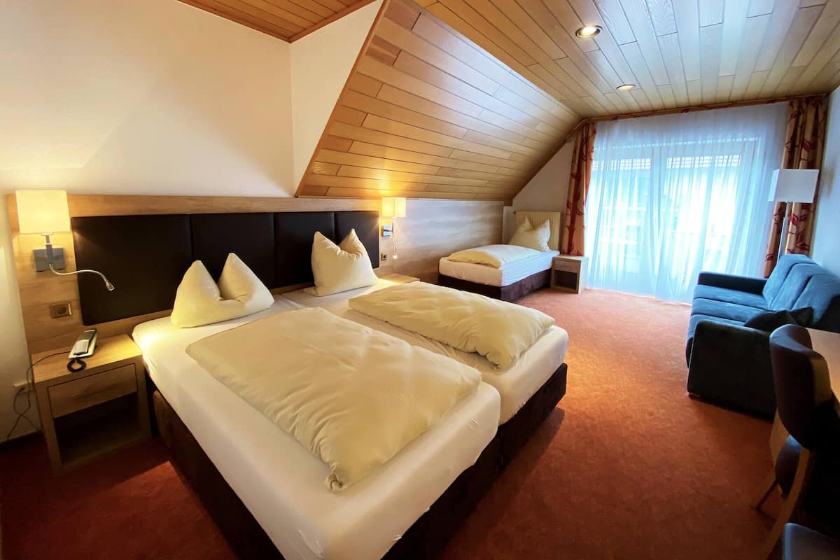A bedroom with a large bed, two bedside tables, a nightstand, a sofa, and a window with curtains.