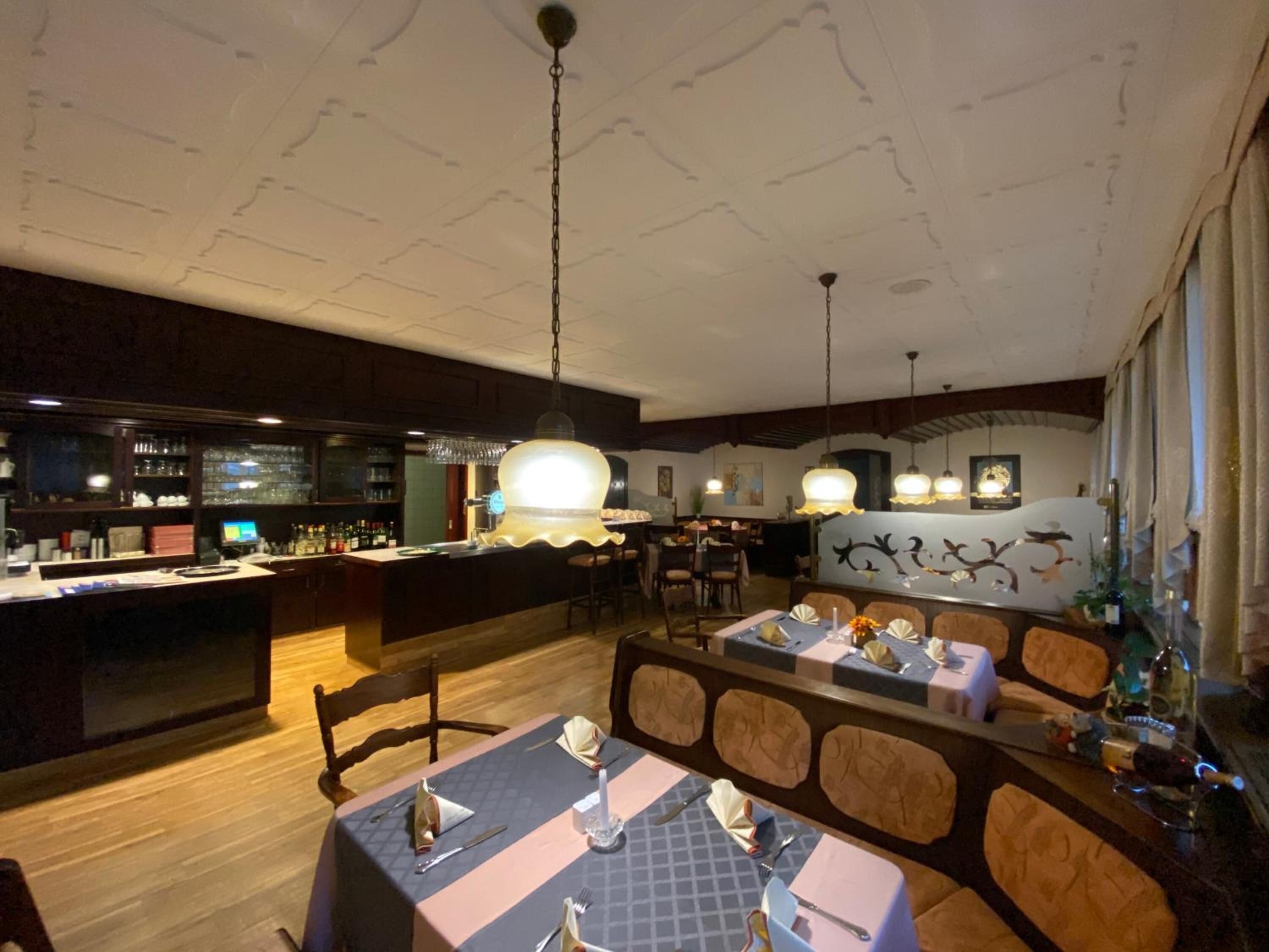 Un restaurante con zona de bar, suelo de madera y techo alto con vigas a la vista.