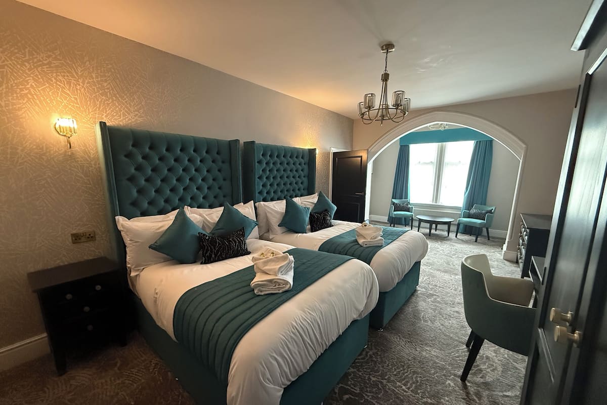 A hotel room with two beds, a chandelier, a seating area with a table, and a view of the outdoors.