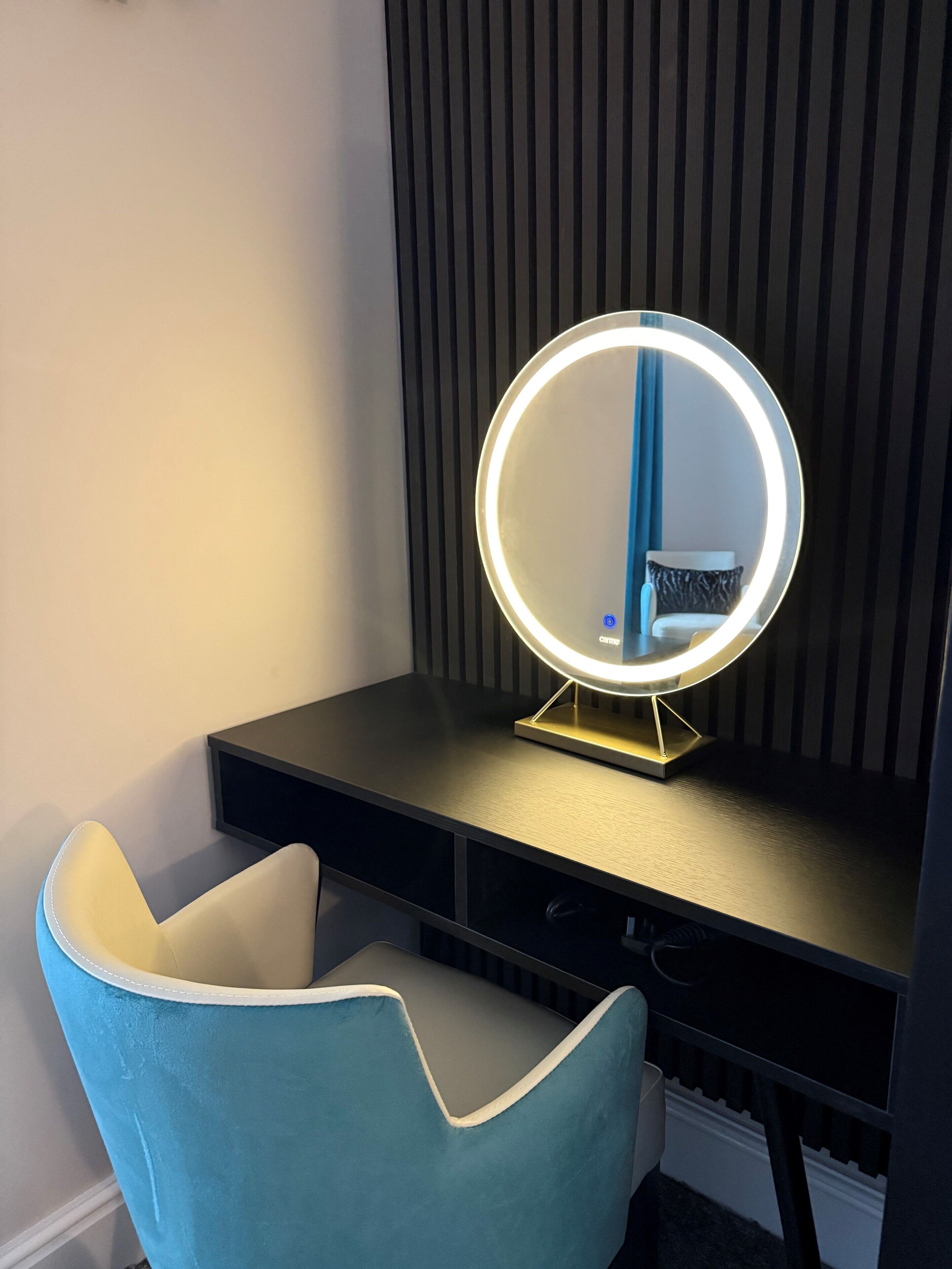 A vanity with a round mirror and a blue chair.