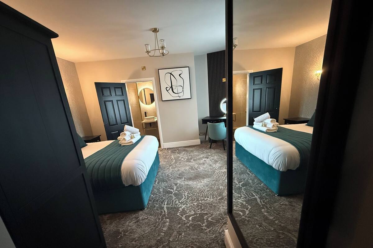 A hotel room with two beds, a desk, a chair, a mirror, and a chandelier.