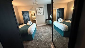 Une chambre d’hôtel avec deux lits, un bureau, une chaise, un miroir et un lustre.