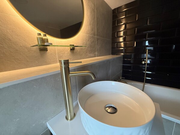 A modern bathroom with a white sink, gold faucet, and a mirror with a gold frame.