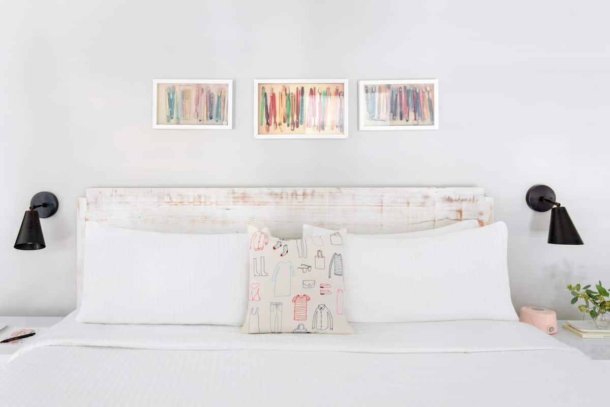 A neatly made bed with white linens, two black bedside lamps, and a pink alarm clock.