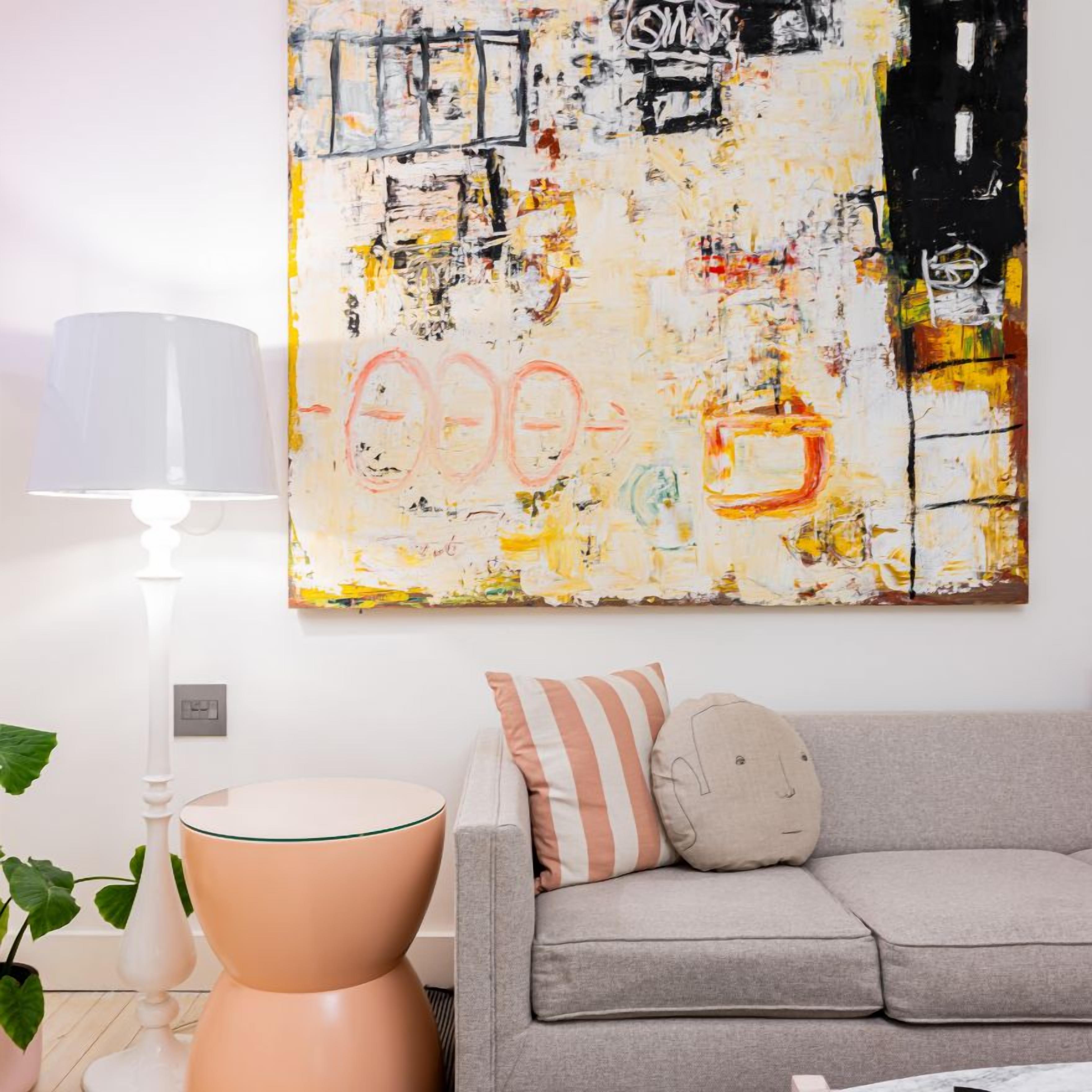 Una sala de estar con un sofá, cojines, una lámpara y un cuadro abstracto grande en la pared.