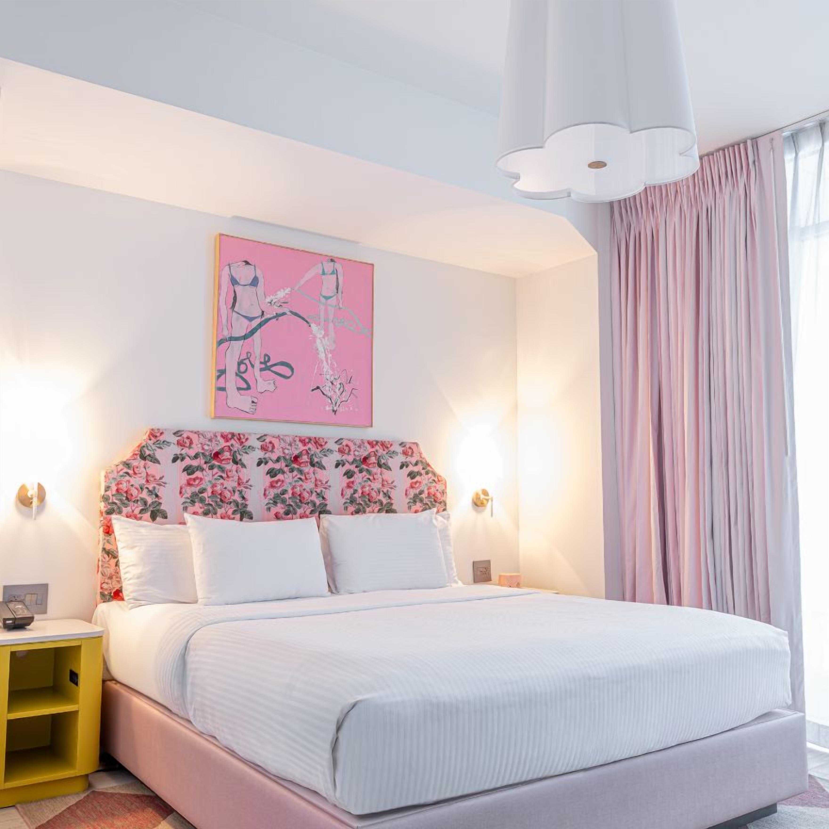 A bedroom with a bed, a nightstand, a wall art piece, and a window with curtains.