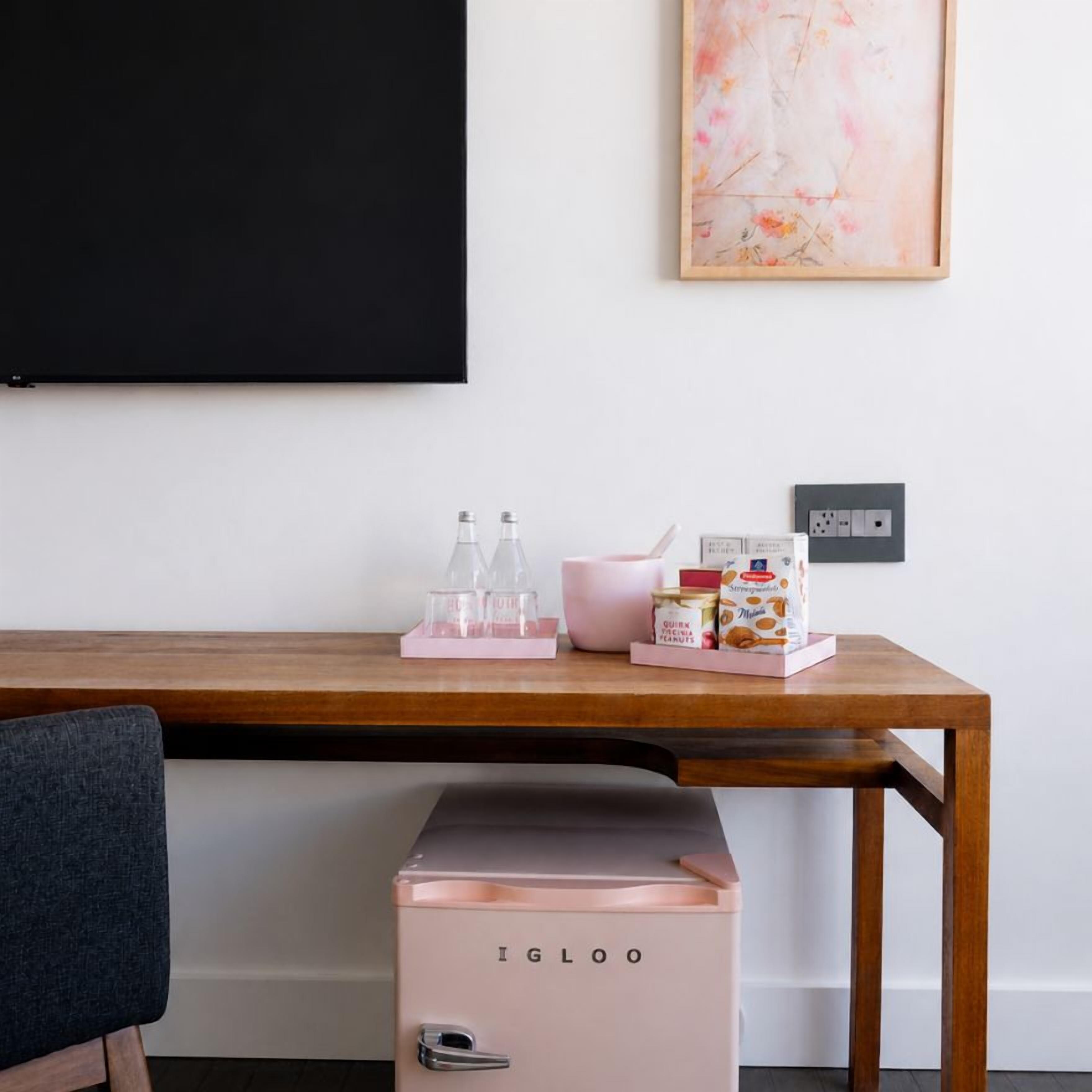 A wooden desk with a pink Igloo refrigerator, a blackboard, and a framed artwork on the wall.