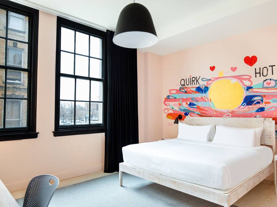 Habitación de hotel con cama, escritorio, silla, ventana y pared con un diseño abstracto colorido.