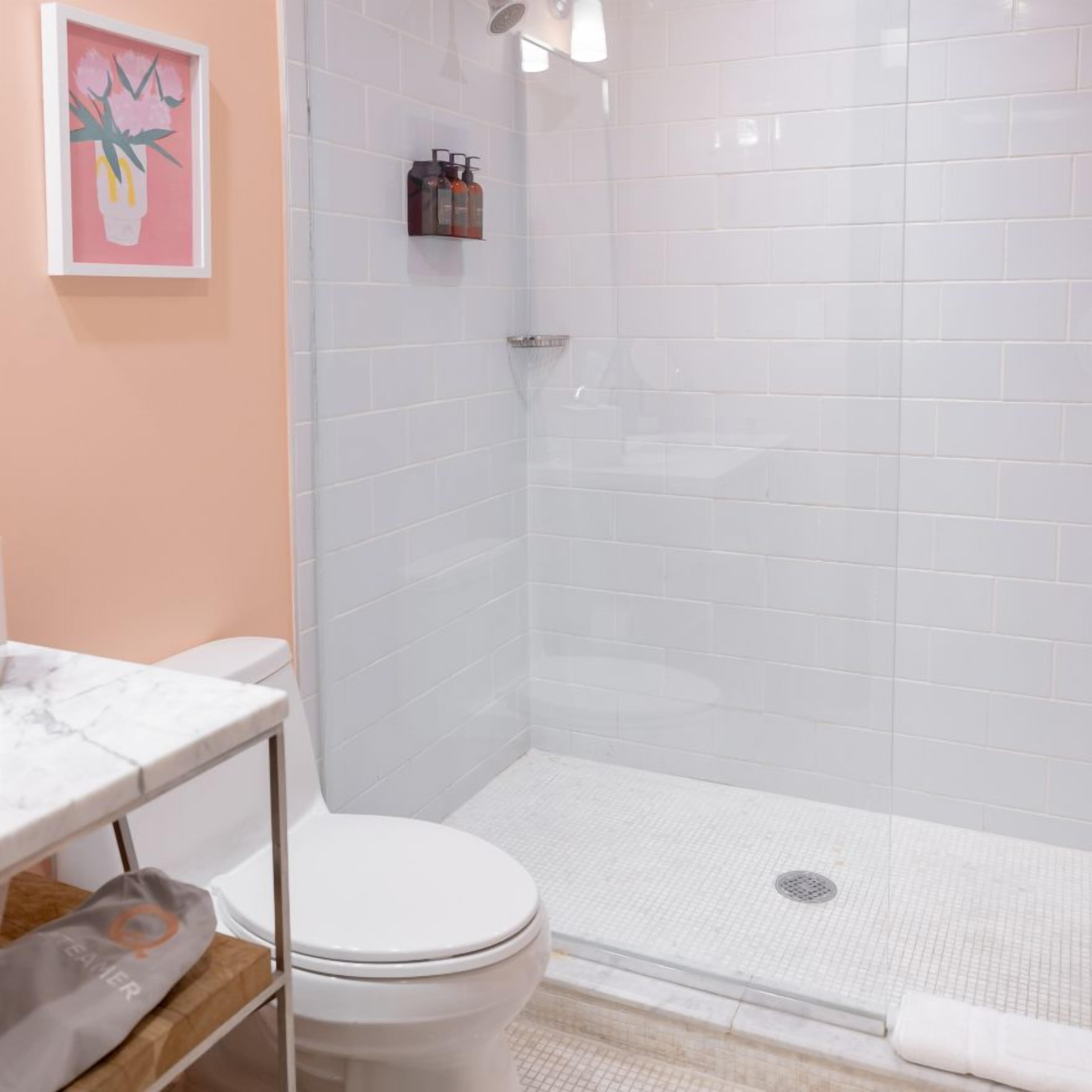 Une salle de bain avec des toilettes blanches, une douche dotée d’une porte en verre et un comptoir en marbre.