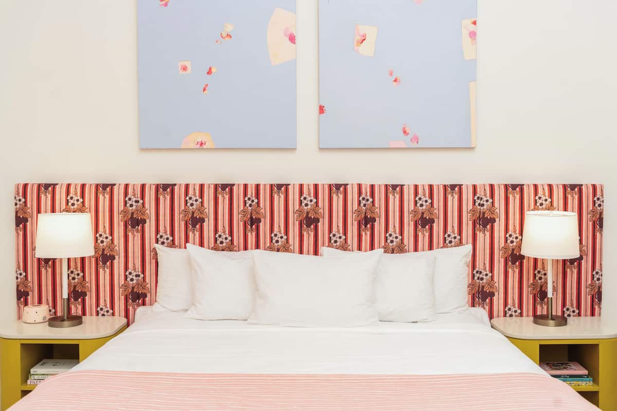 A hotel room with a bed, two bedside tables with lamps, a striped floral headboard, and two wall-mounted artworks.