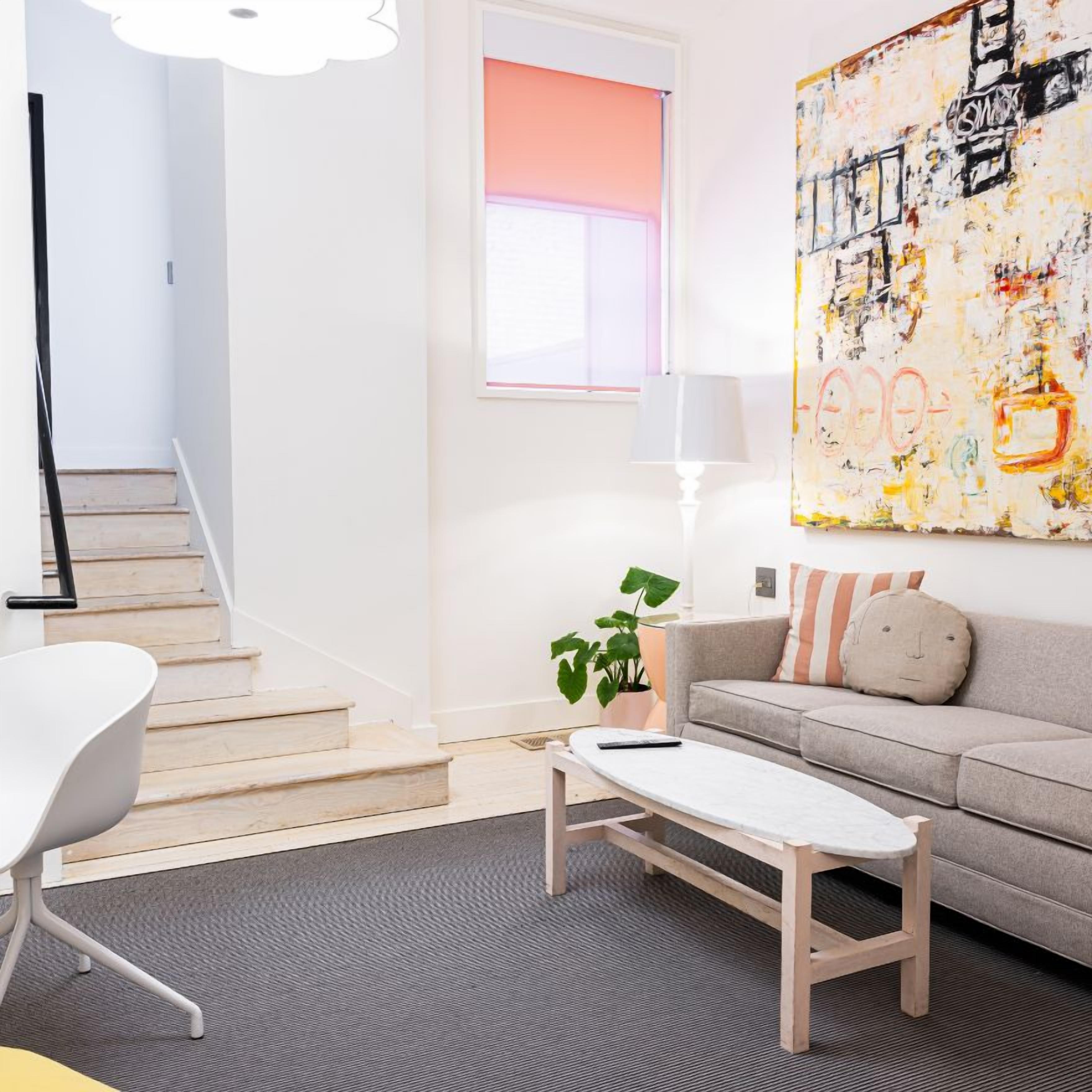Un salon moderne avec un escalier, un canapé, une table basse et un grand tableau abstrait.