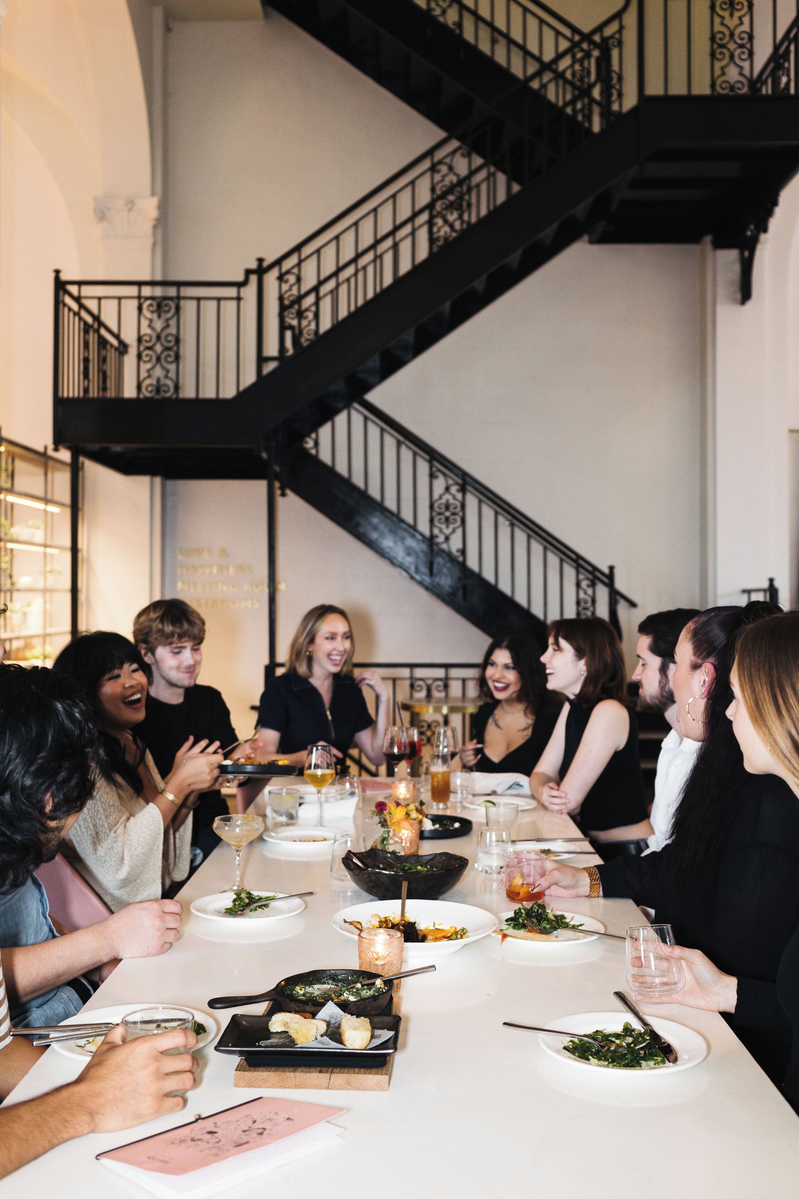 Un grupo de personas cenando en una mesa, con una escalera al fondo.