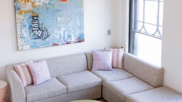 Un salon moderne avec un canapé d’angle, un pouf rond et un grand tableau abstrait accroché au mur.