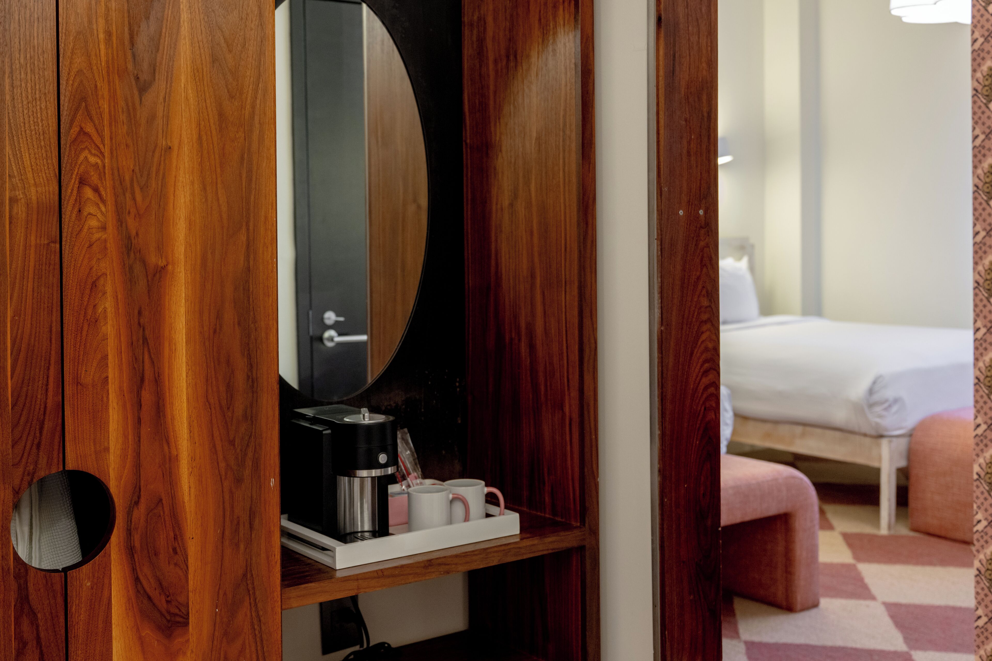 A wooden wardrobe with a mirror, a coffee maker, and two mugs on a shelf.