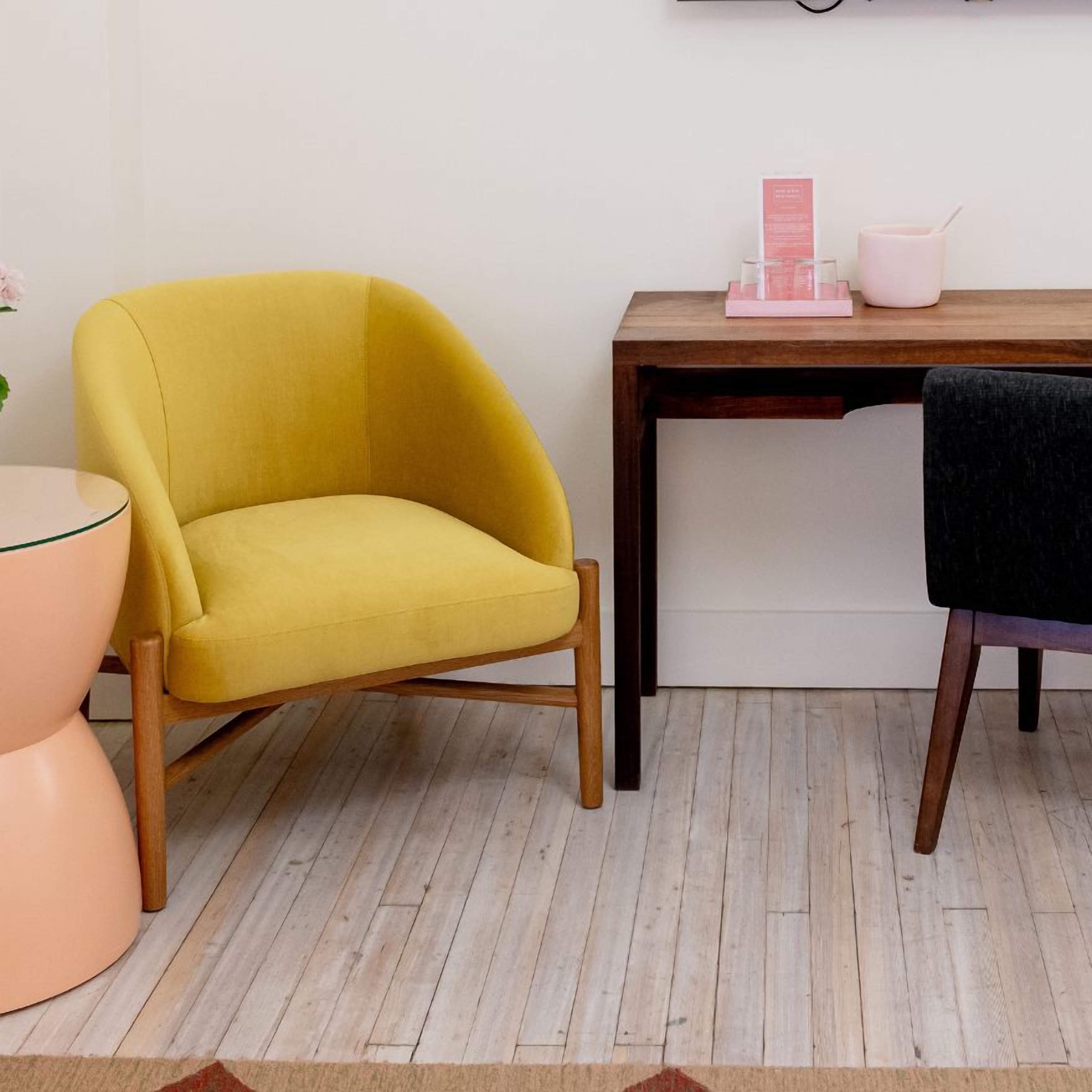 A room with a yellow armchair, a wooden desk, a pink side table, and a small plant.