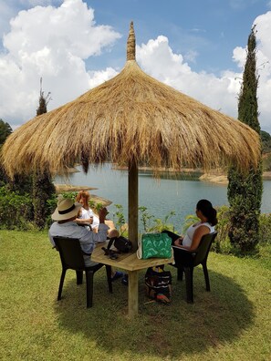 A thatched umbrella table with four people seated around it, overlooking a body of water. - Hotel Pietrasanta (El Peñol)