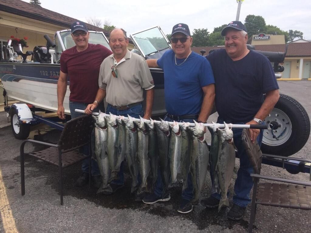 Four men standing next to a boat with a trailer, holding a line of fish.