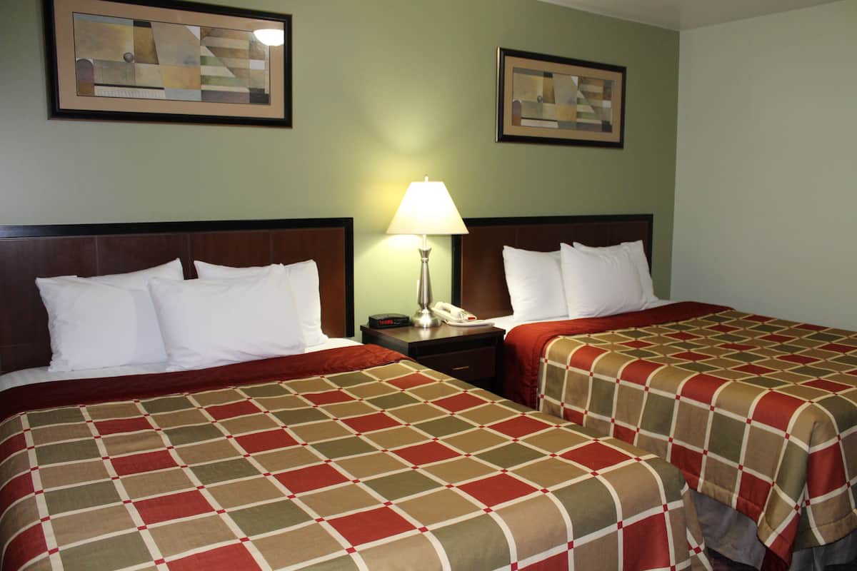 A hotel room with two beds, a nightstand with a lamp, and artwork on the walls.