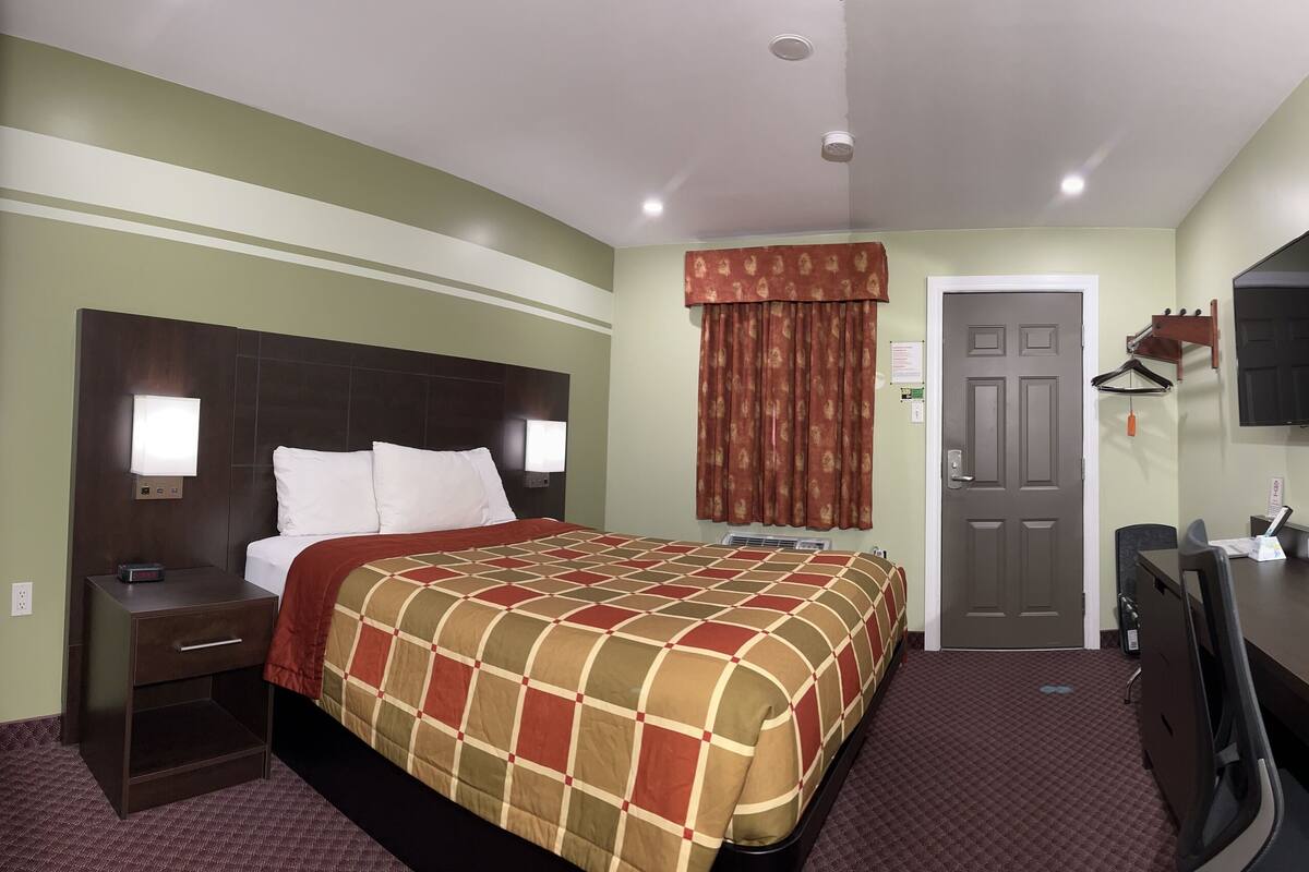 A hotel room with a bed, bedside table, dresser, mirror, and a door.