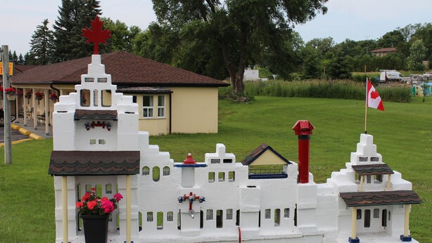 A model of a white building with a red maple leaf on top, surrounded by green grass. - Budget Inn Port Hope (Port Hope)