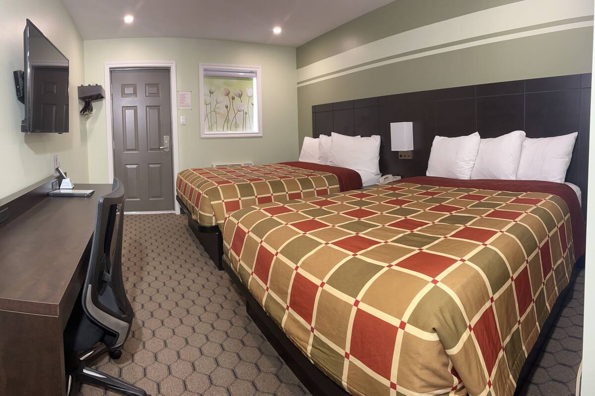 A hotel room with two beds, a desk, a chair, a mirror, and a door.