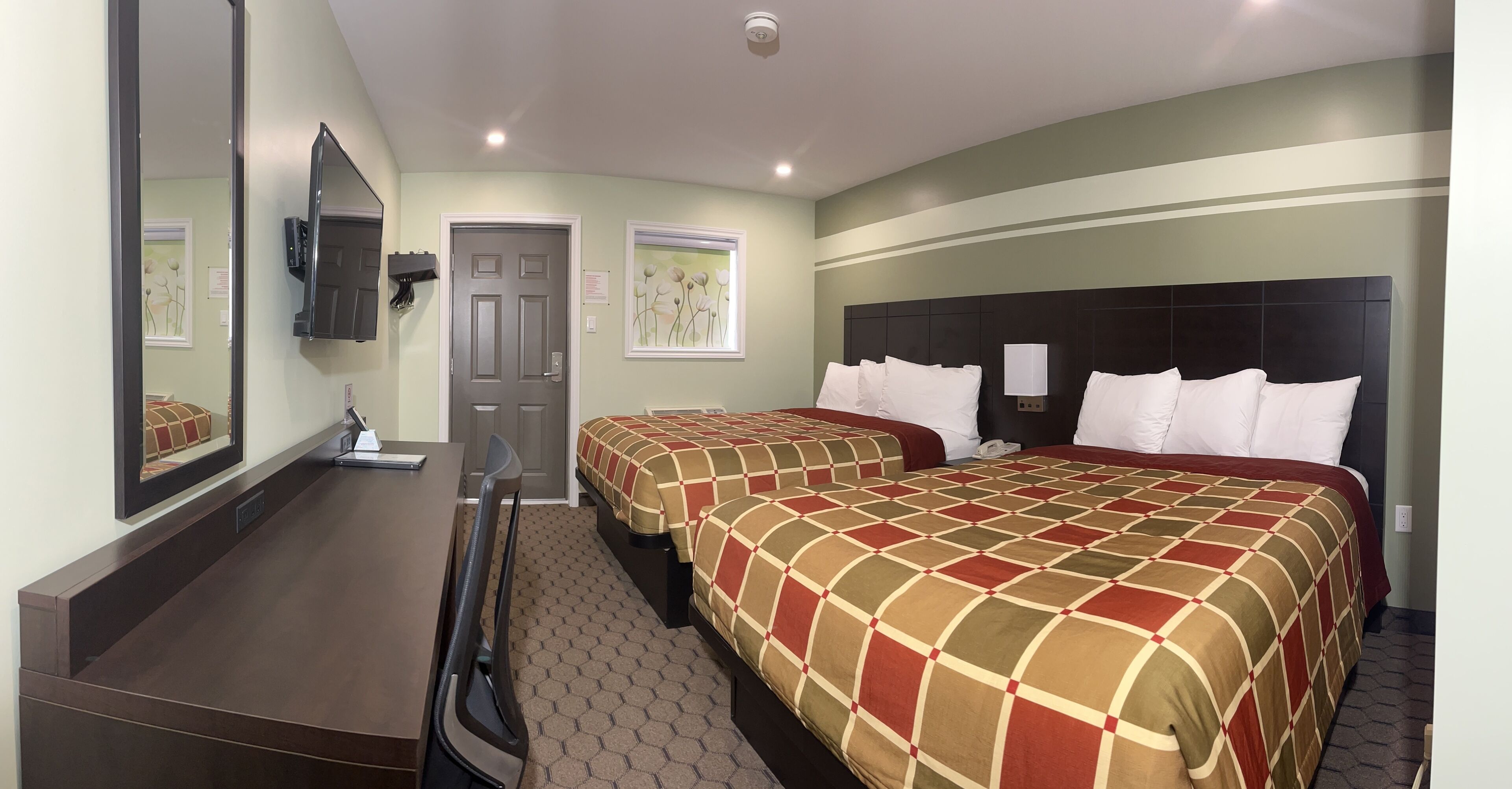 Una habitación de hotel con dos camas, un escritorio, un espejo y una puerta.