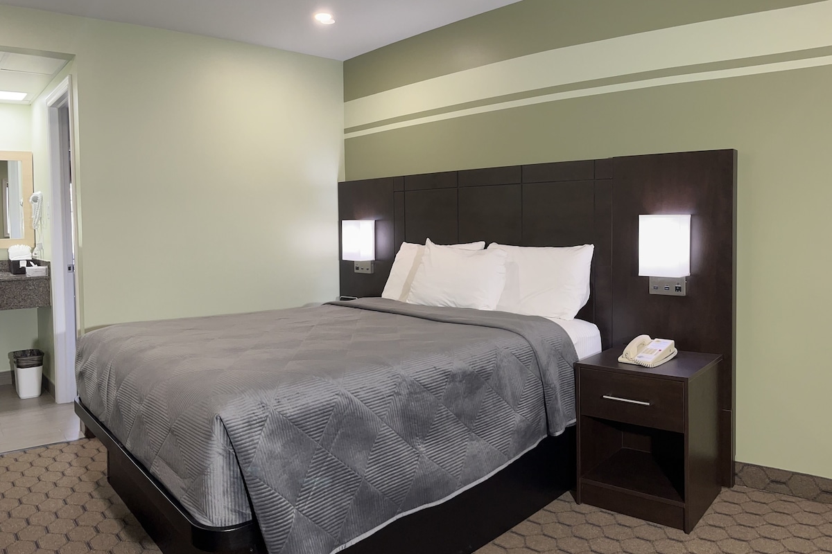 A hotel room with a large bed, a bedside table with a phone, and a nightstand with a lamp.