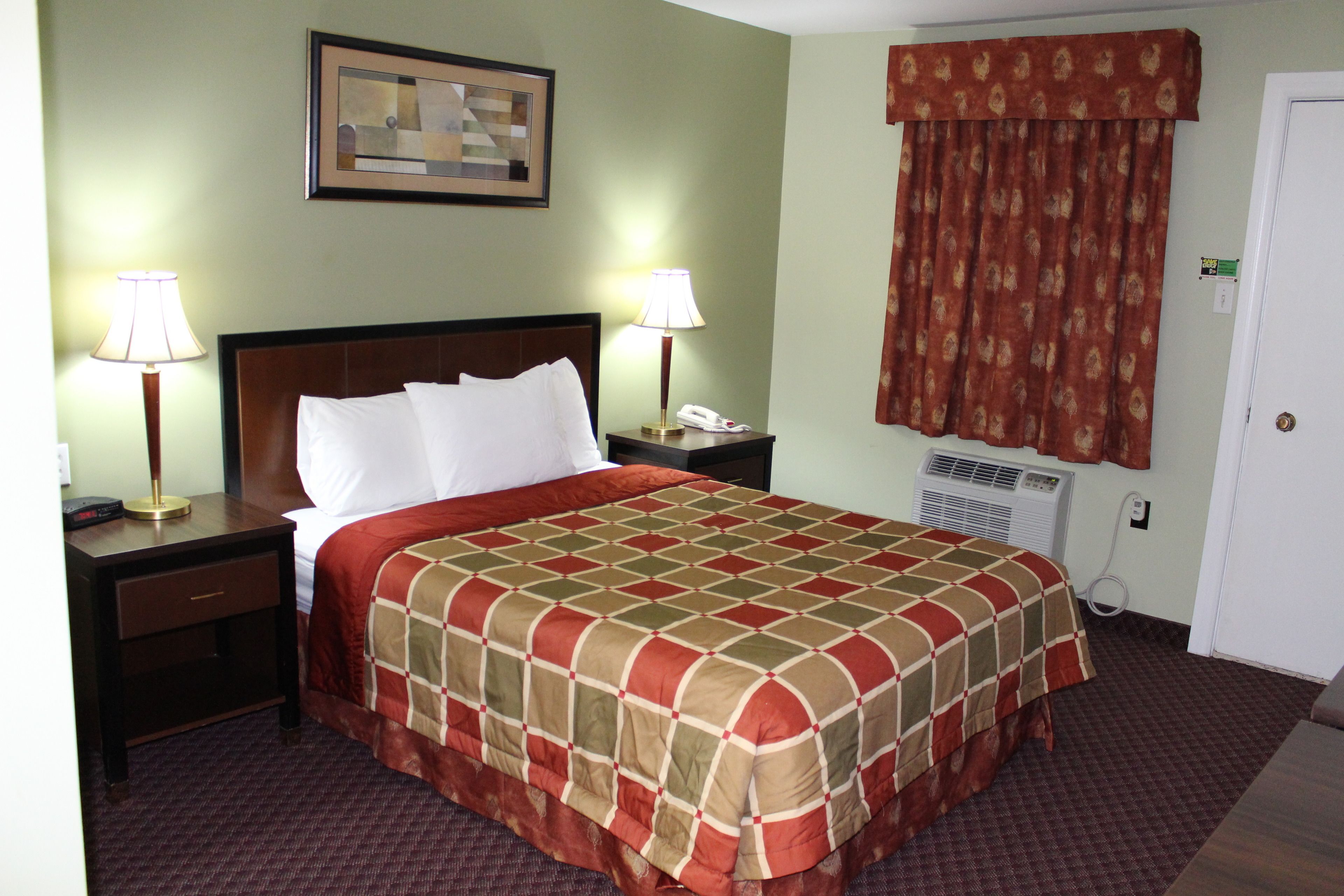 Habitación de hotel con una cama grande, dos mesitas de noche con lámparas, un cuadro en la pared, una ventana con cortinas y un termostato en la pared.