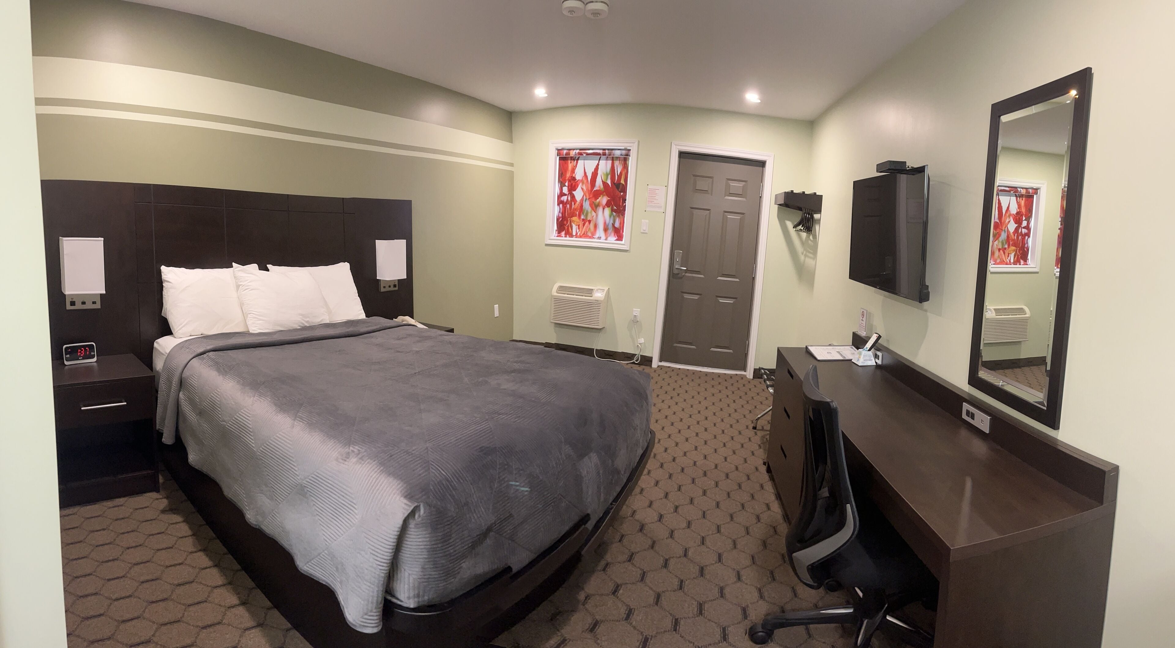 Una habitación de hotel con cama, escritorio, silla, televisor y espejo.