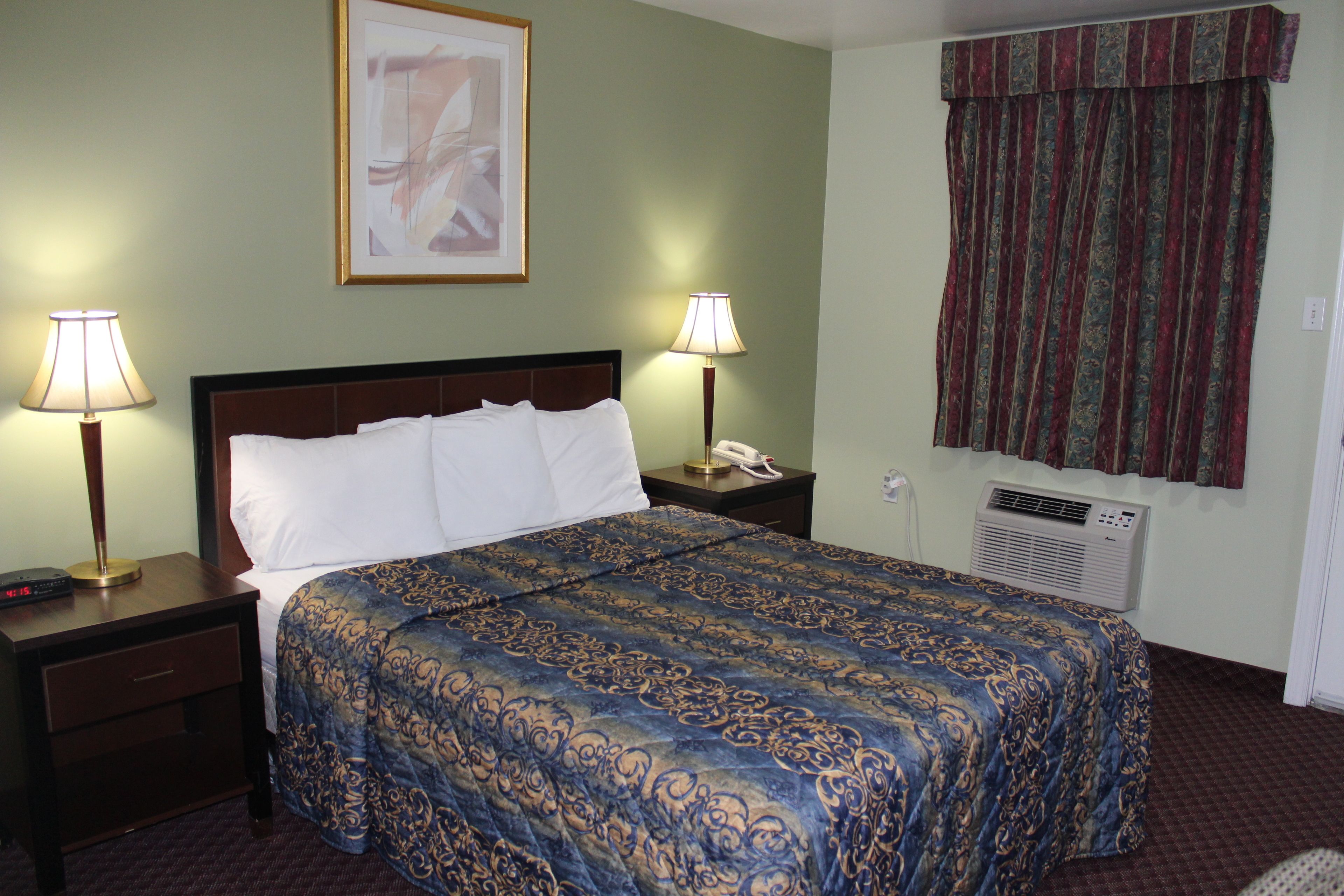 Habitación de hotel con una cama bien hecha, dos lámparas de noche, una mesita de noche con teléfono y un aire acondicionado de pared.