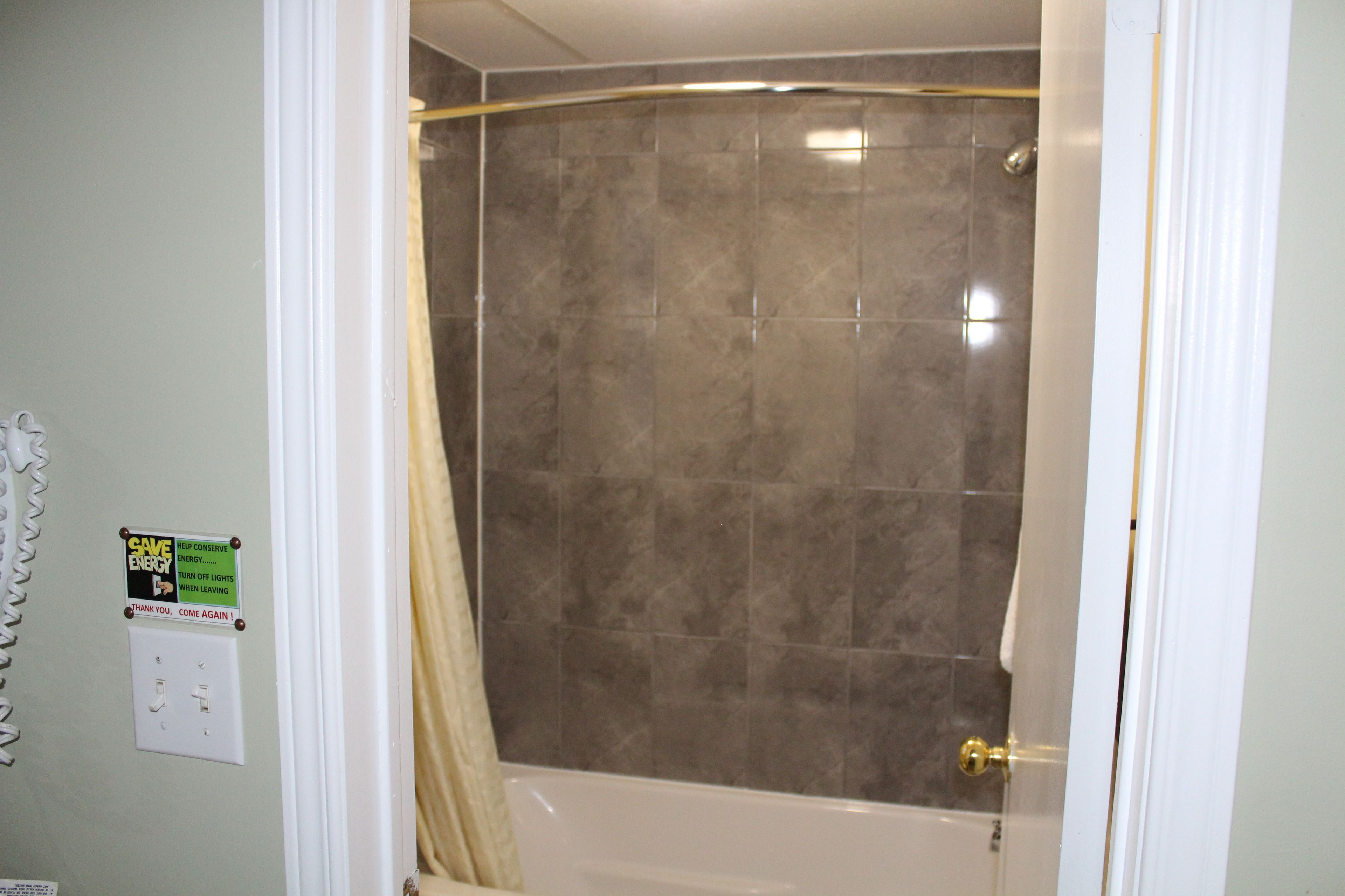 A bathroom with a shower, a towel rack, and a sign encouraging energy conservation.