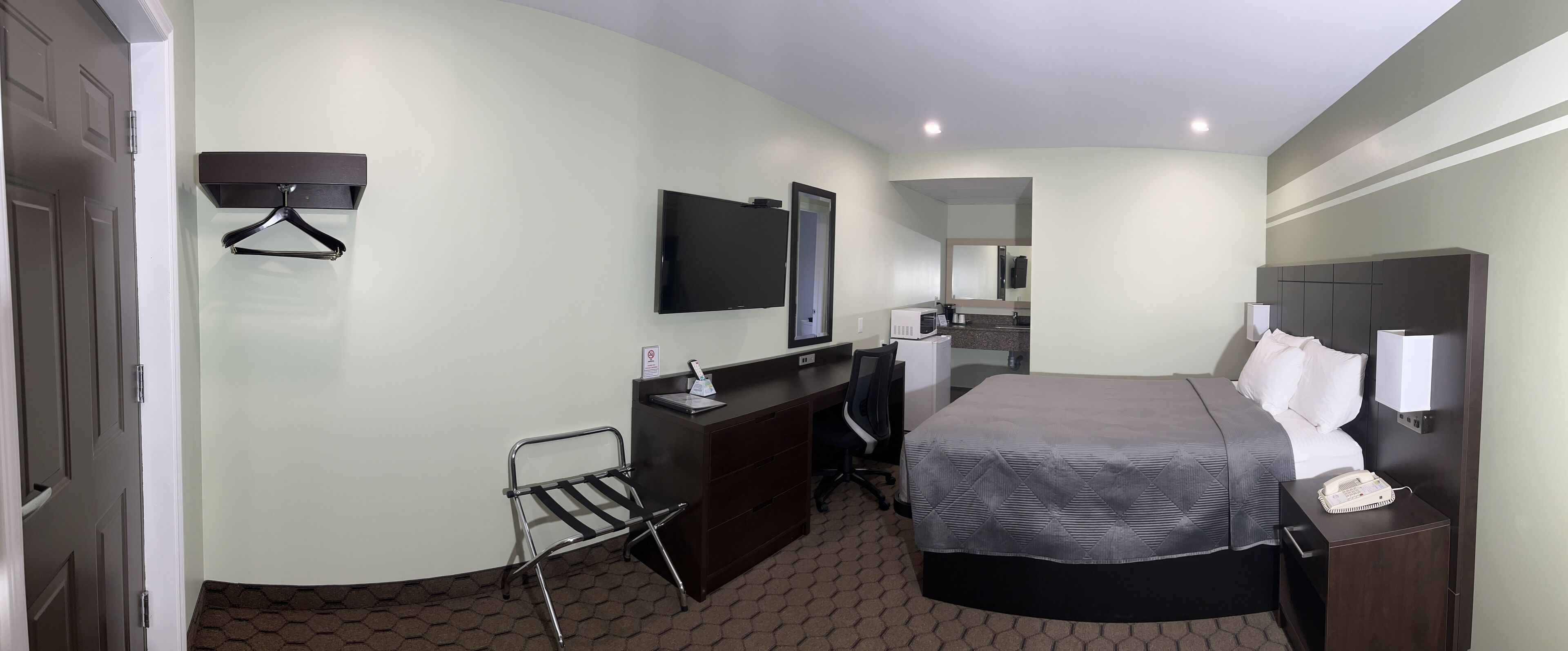 A hotel room with a bed, a desk, a chair, a TV, and a mirror.