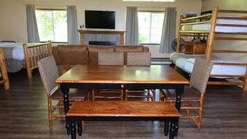 A room with a wooden dining table, cushioned seating, a bunk bed, a television, and a fireplace.