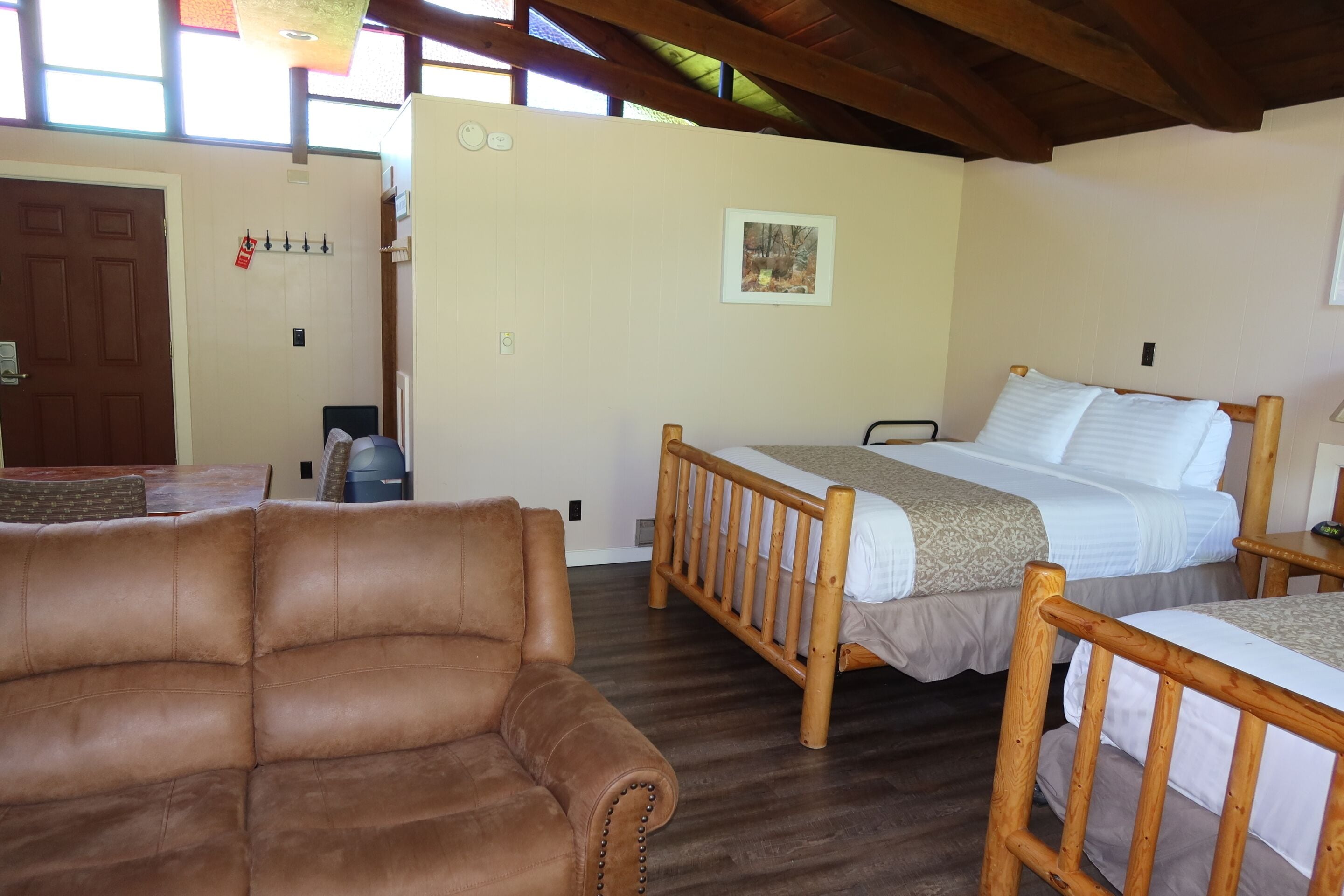 A room with a brown leather sofa, a wooden bed with a headboard, a wooden table, and a framed picture on the wall.
