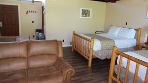 A room with a brown leather sofa, a wooden bed with a headboard, a wooden table, and a framed picture on the wall. - Mountain View Lodge (Packwood)