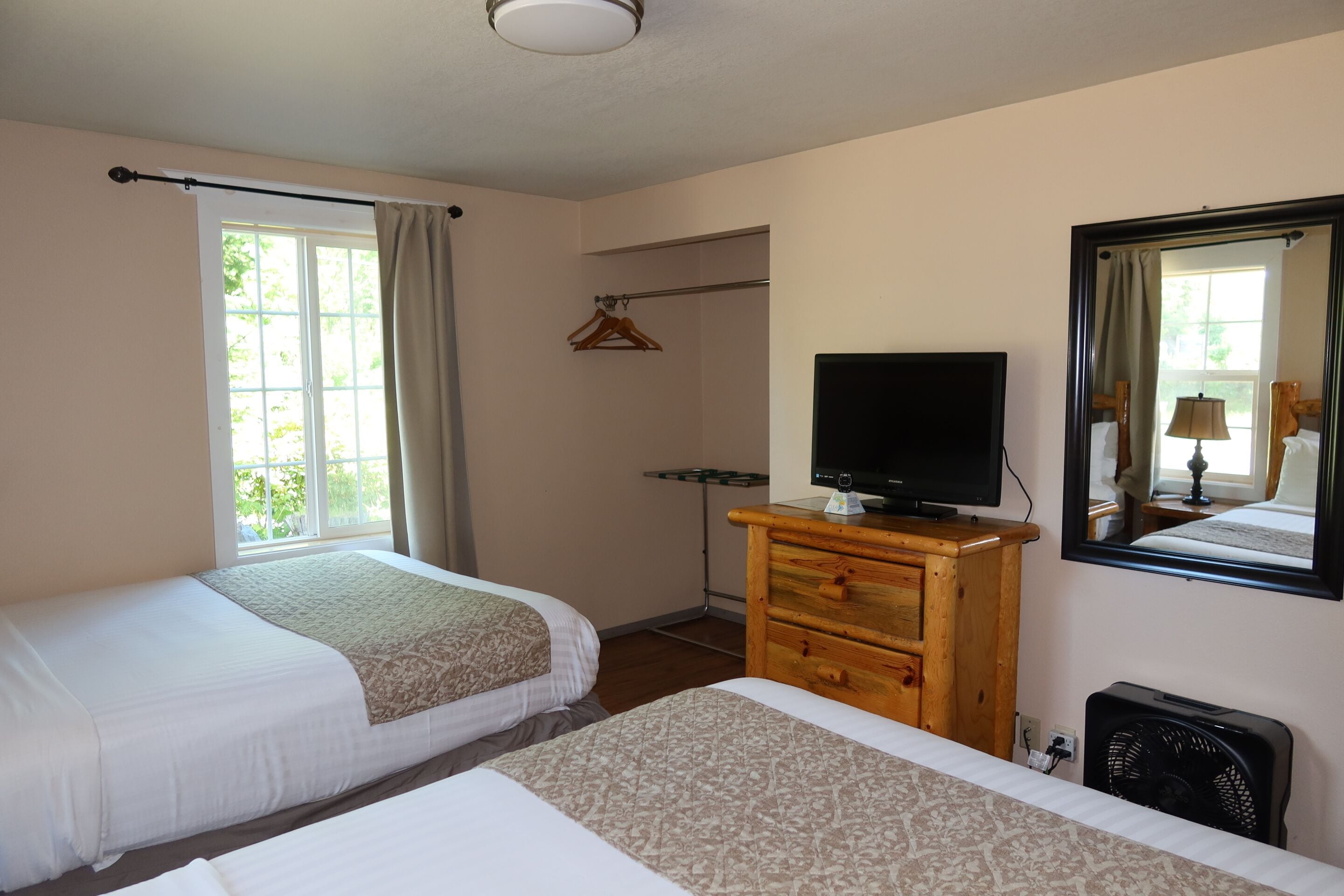 A hotel room with two beds, a TV, a dresser, a mirror, and a window with curtains.