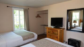 A hotel room with two beds, a TV, a dresser, a mirror, and a window with curtains.