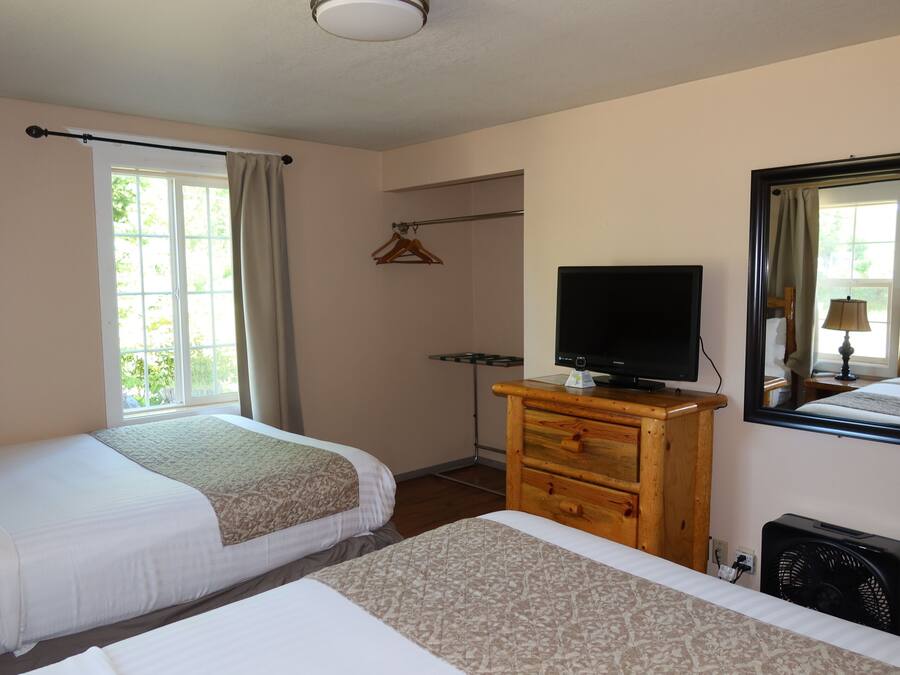 A hotel room with two beds, a TV, a dresser, a mirror, and a window with curtains.