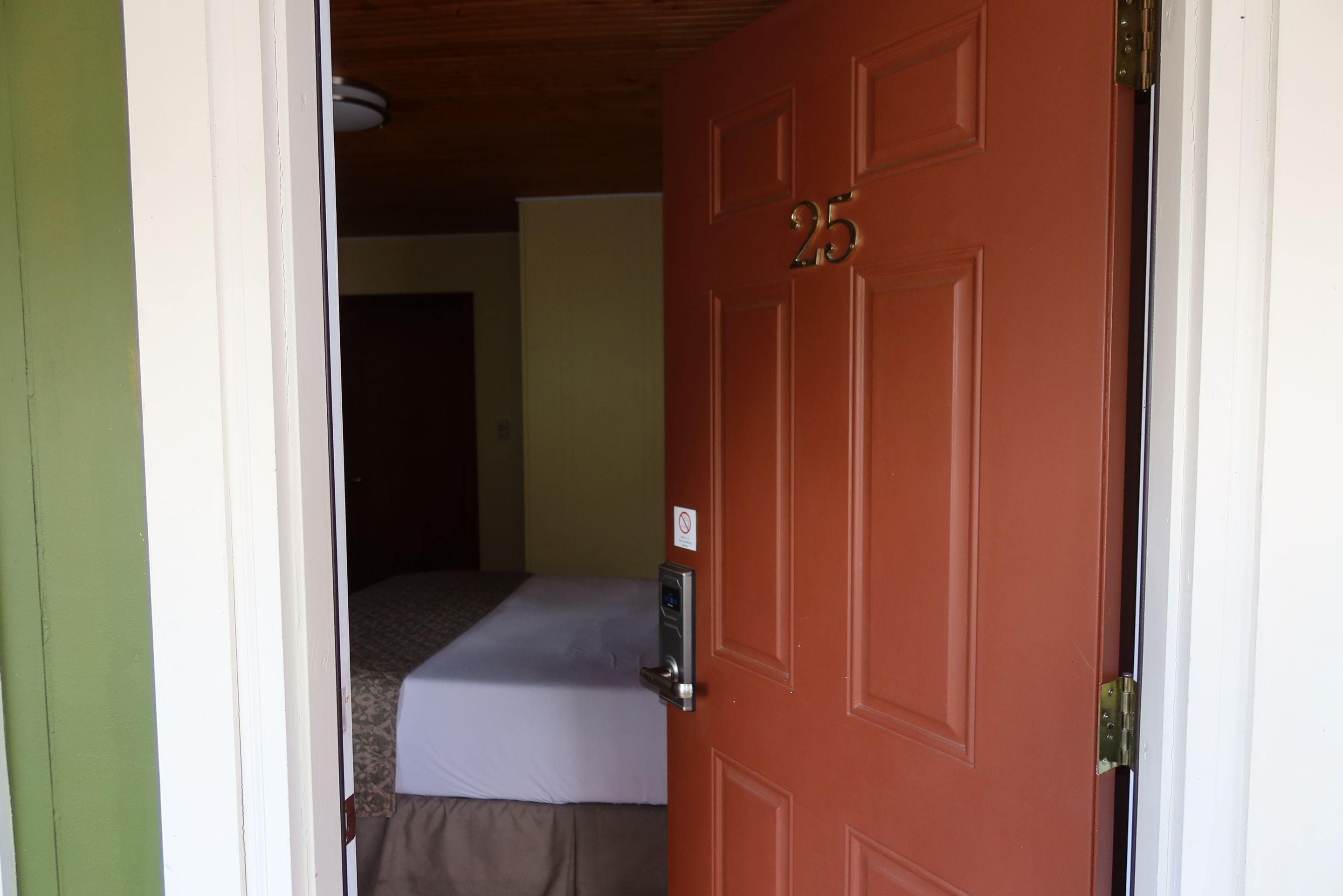 Una habitación con una cama, una puerta con el número 25 y una mesita con una lámpara.