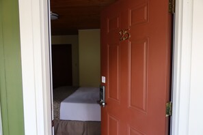 Une chambre avec un lit, une porte portant le numéro 25 et une petite table avec une lampe.