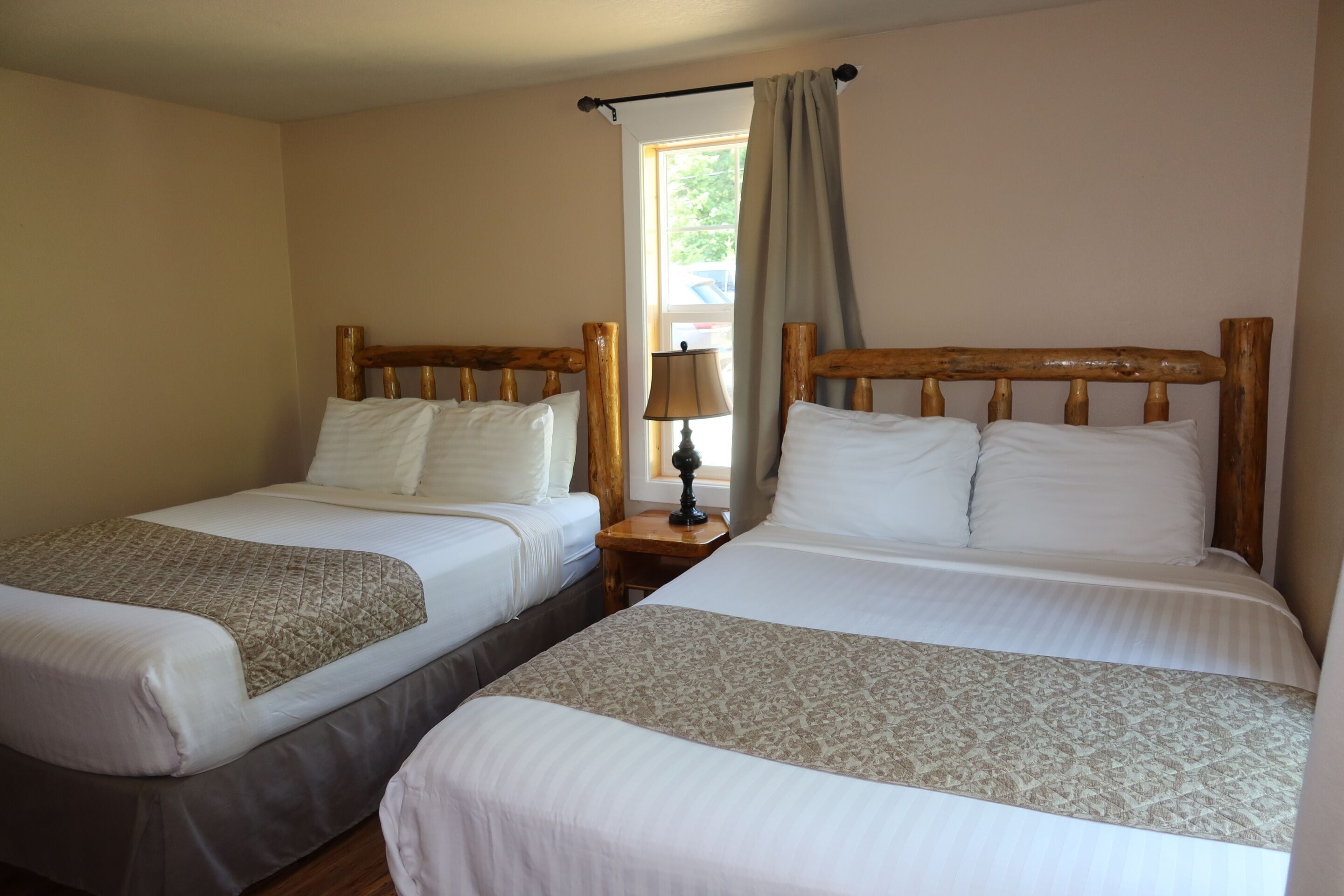 A room with two single beds, a nightstand with a lamp, and a window with curtains.