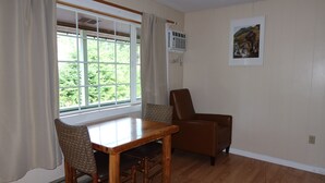 A room with a dining table, two chairs, a brown leather chair, a window with curtains, an air conditioning unit, and a framed picture on the wall. - Mountain View Lodge (Packwood)
