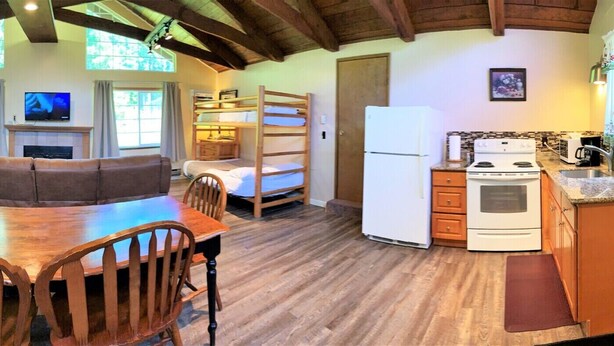 A cozy cabin interior with a dining table, wooden chairs, a sofa, a kitchen with a stove and refrigerator, and a fireplace. - Mountain View Lodge (Packwood)
