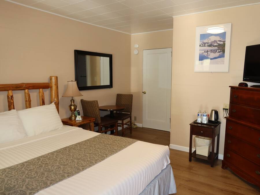 Habitación de hotel con cama, escritorio, silla, cómoda, televisor y un cuadro en la pared.