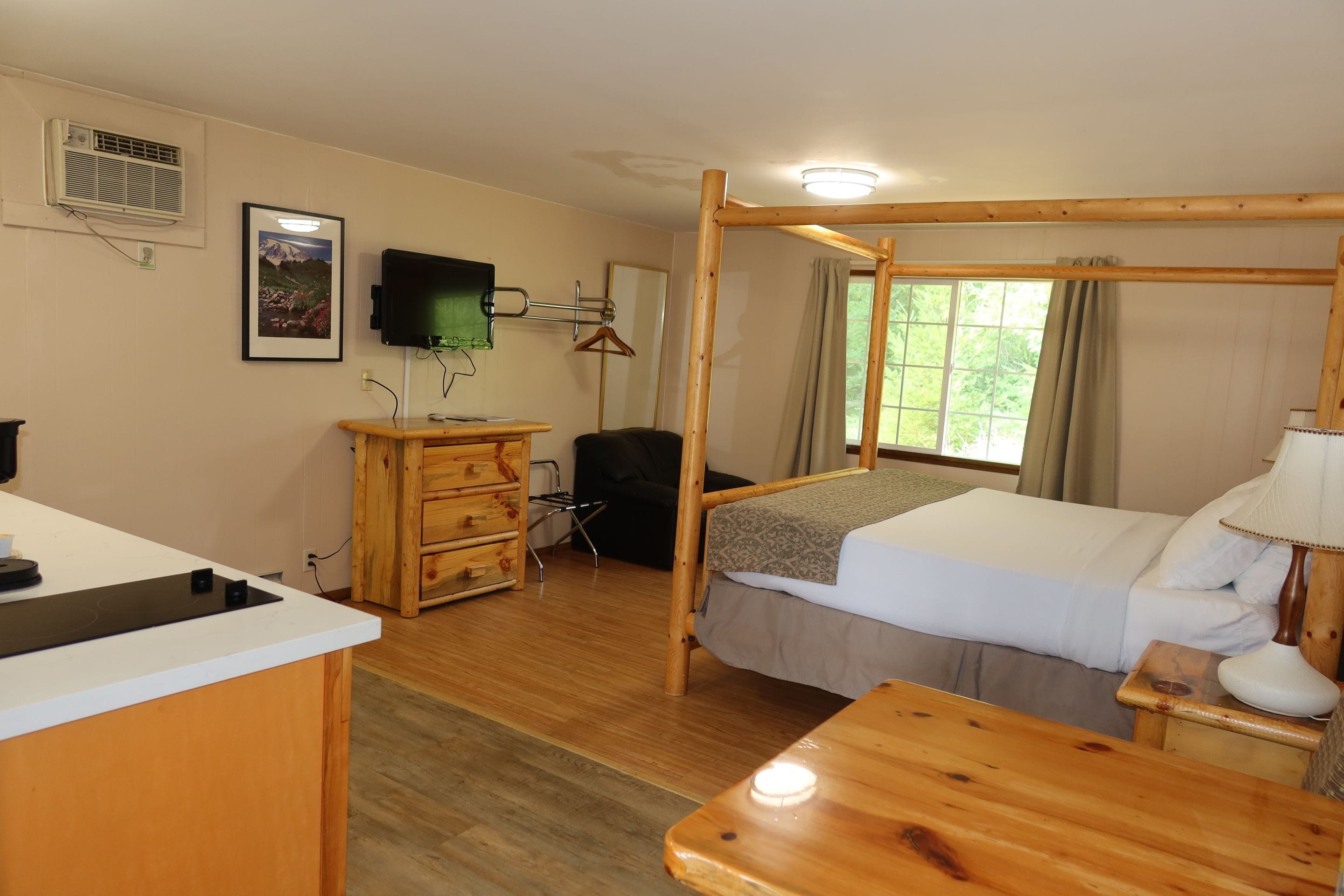 A hotel room with a wooden bed, a desk with a computer, a TV, and a window with curtains.
